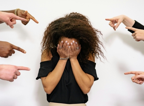 woman with face in hands other hands pointing at her