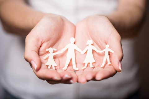 hands holding paper cutouts of a family