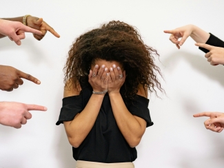 woman with face in hands other hands pointing at her